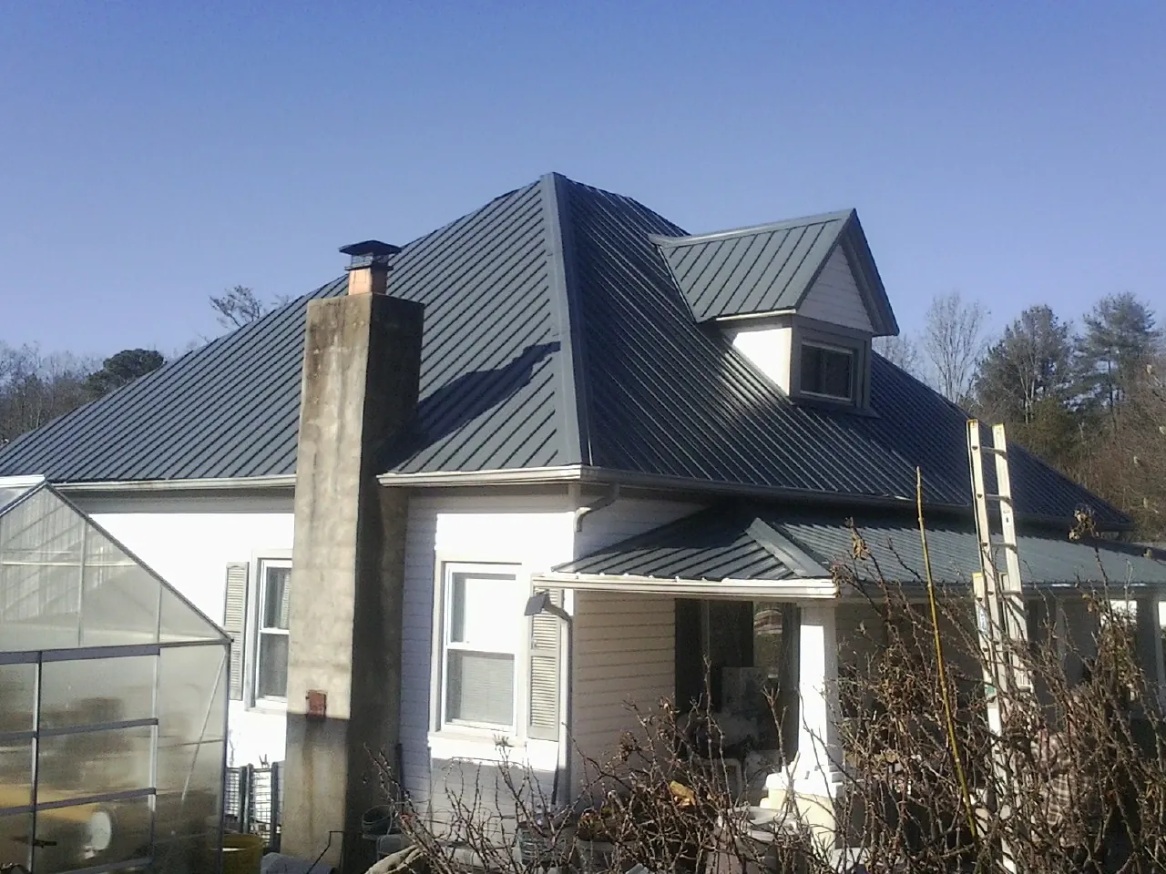 Dark blue standing seam metal roof on a white farmhouse with dormer — Slate & Tile Roof Repair by Roofing Brothers in Oakham