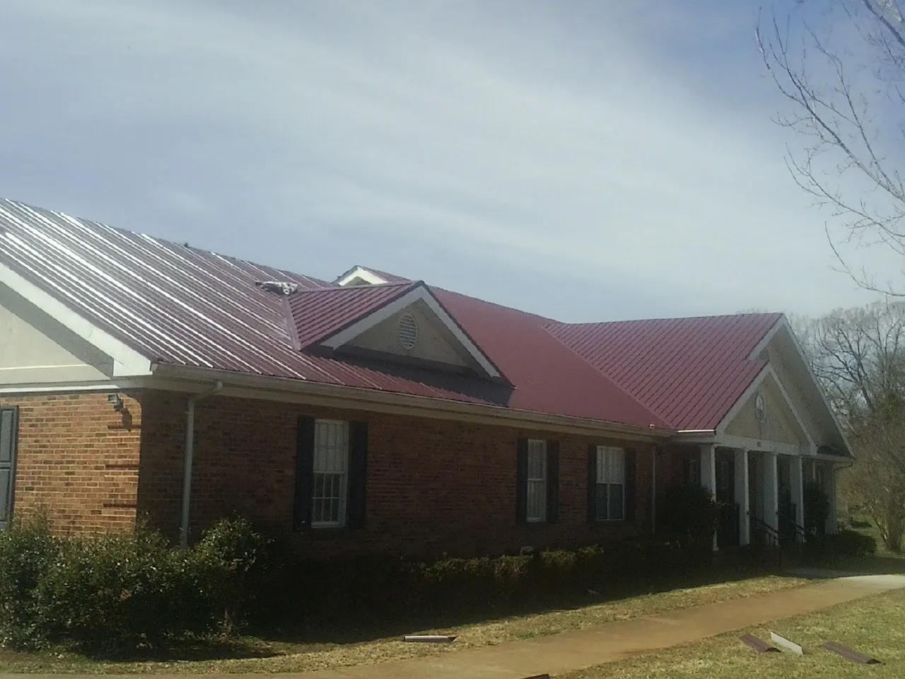 Red metal roof with gabled entries on a long brick building, from a Hail Damage Roof Repair job in Oakham