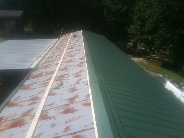 Old rusted panels beside newly installed green metal roofing — Wind Damage Roof Repair by Roofing Brothers in Oakham