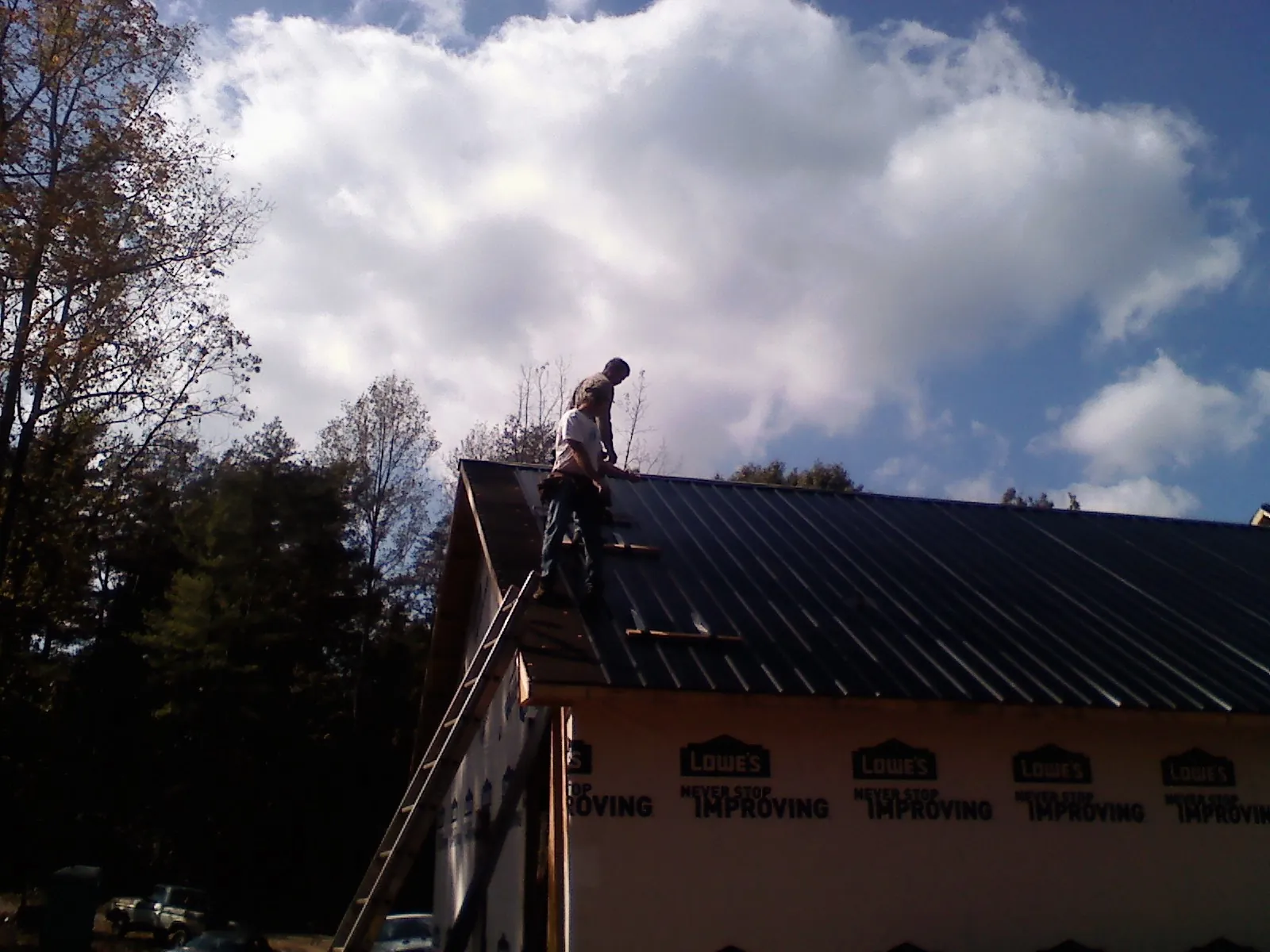 Roofer fastening dark metal panels high against a cloudy sky, from a Roof Inspection job in Oakham