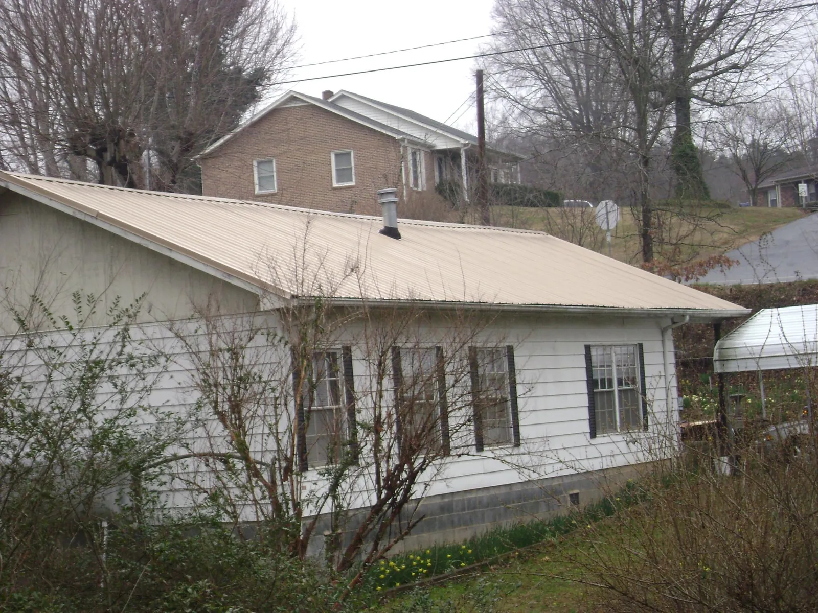 Tan metal roof on a white sided house set into a hillside — Commercial Roofing by Roofing Brothers in Oakham