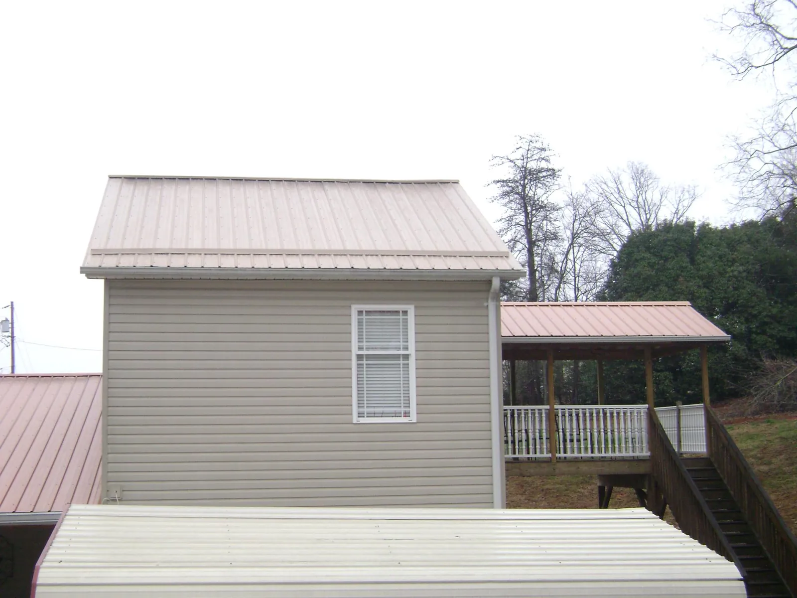 Tan metal roofs on a two story addition and attached porch, from a Roof Replacement job in Oakham